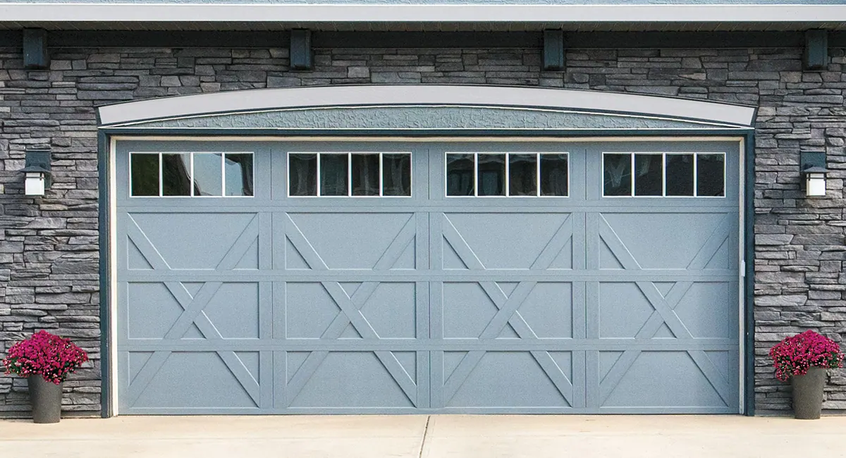 blue carriage house garage door on a house with red flowers in pots