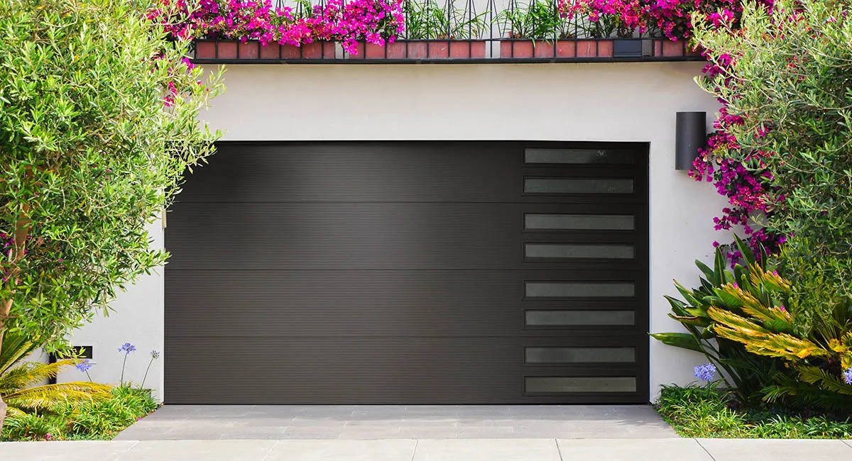 black garage door with flowers and greenery around a home